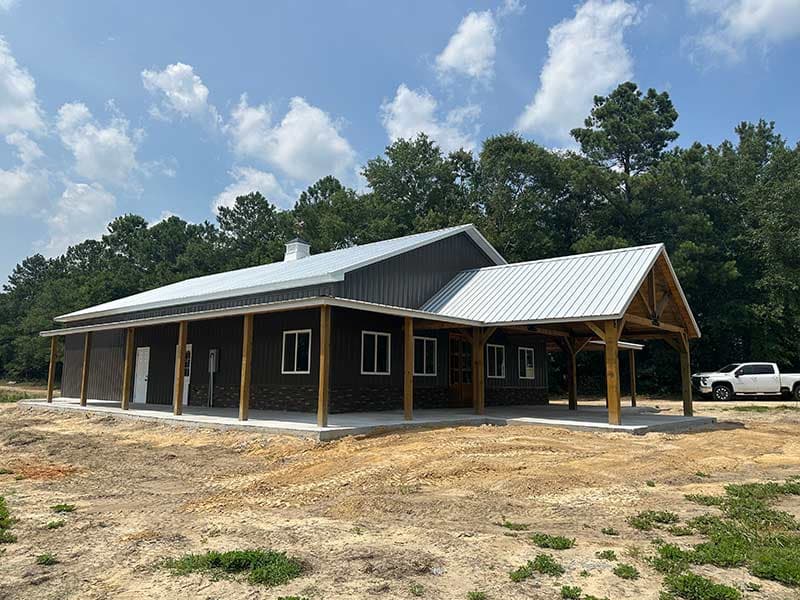 Single-story barndominium with dark siding, a metal roof and a long timber-post porch