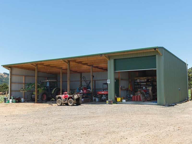 Green post-frame building with an open equipment bay holding a tractor and ATVs