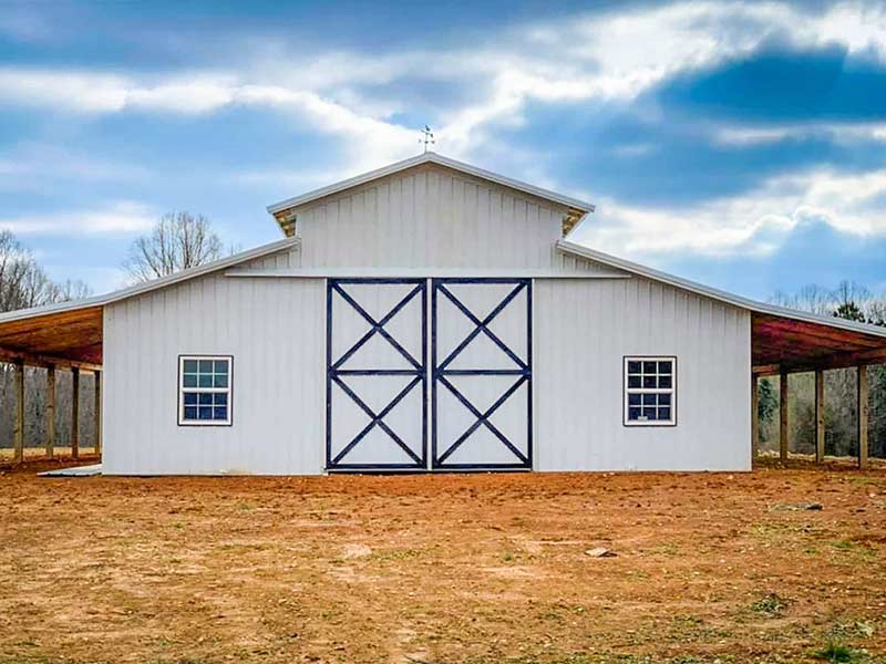 White barn with navy X-braced sliding doors and open sheds on both sides