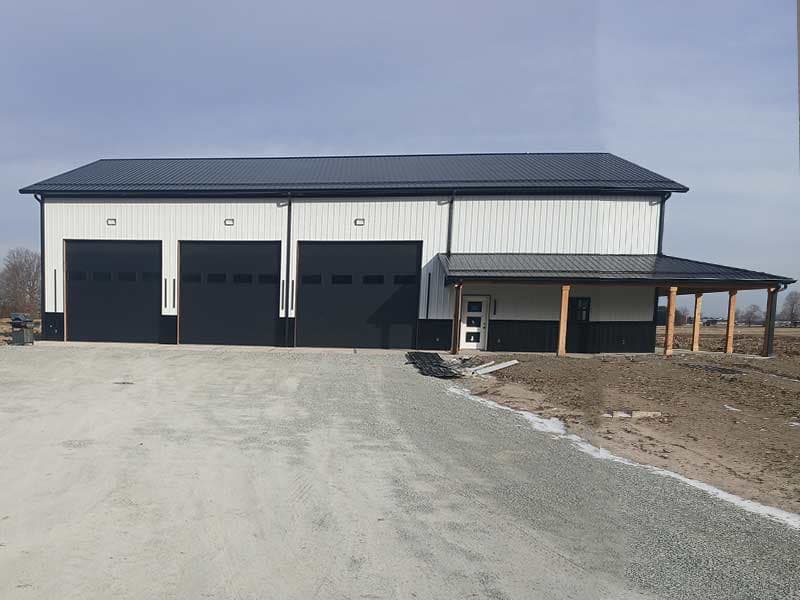 White steel shop with three black overhead doors and an attached covered porch