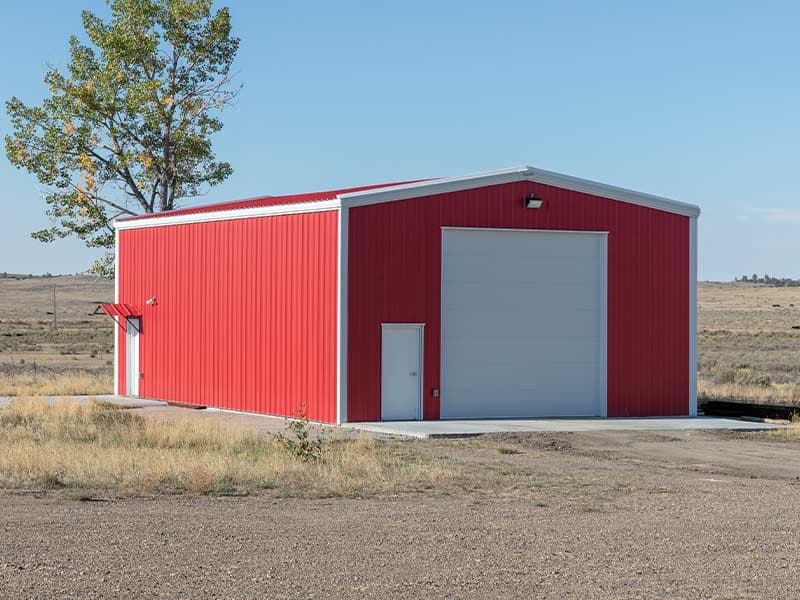 Red and white steel building with a large roll-up door on open land