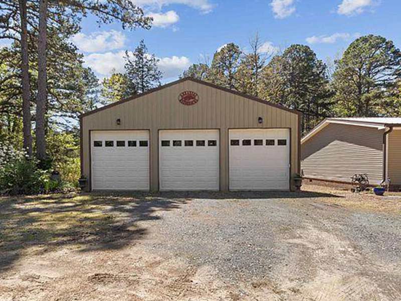 Tan three-car metal garage among pine trees