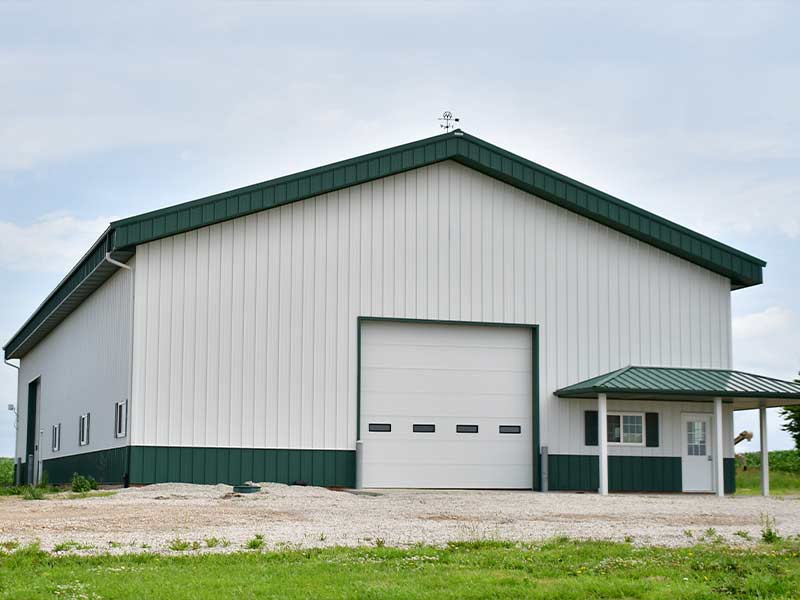 White steel building with green trim, a large overhead door and a covered entry
