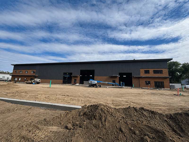 Dark commercial metal building beyond a graded construction site