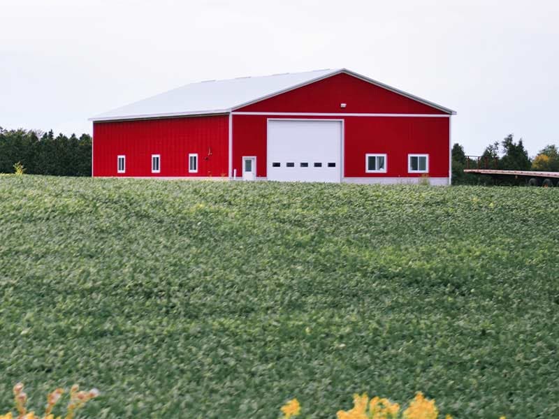 Red pole barn with a white overhead door across a green field