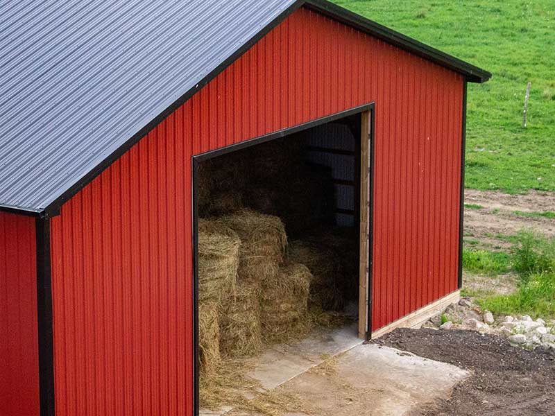 Corner of a red pole barn with hay bales visible inside the open door