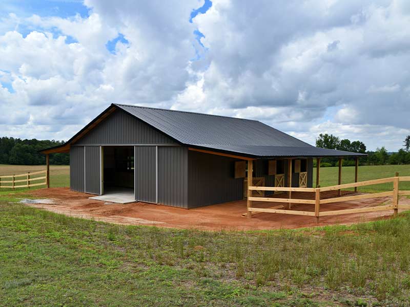 Charcoal post-frame barn with a covered side porch and wood fencing
