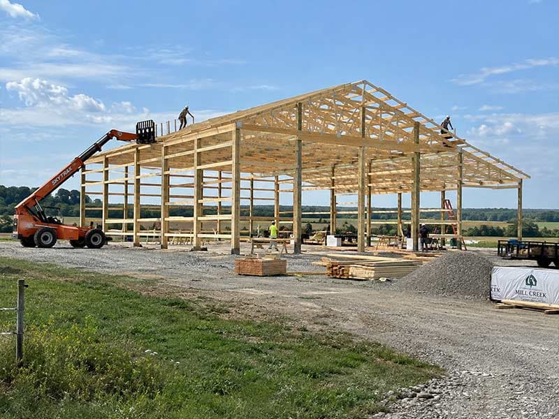 Post-frame building under construction with a lift raising roof trusses