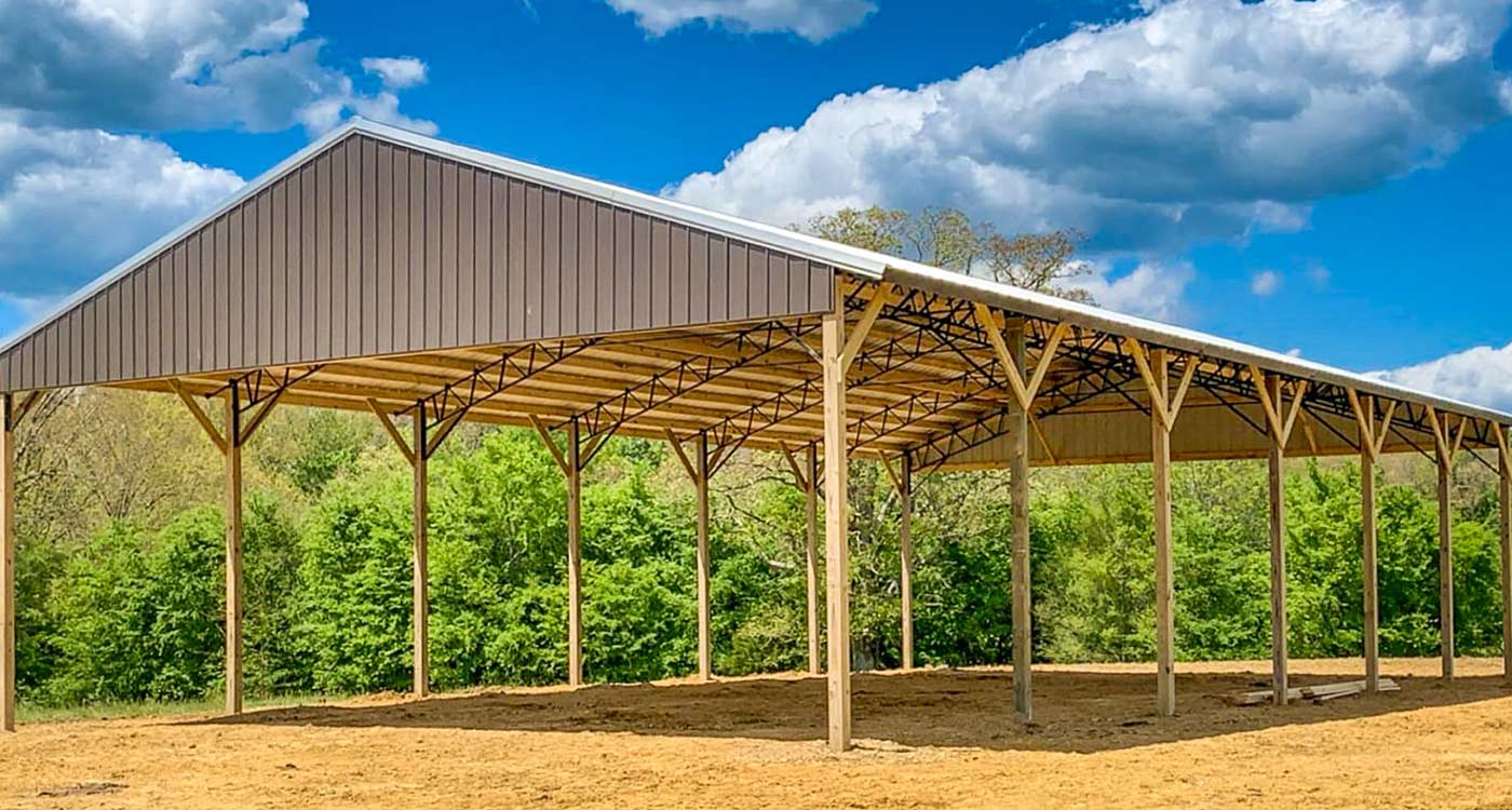 Open-sided wood pole shelter with a steel roof on a dirt pad