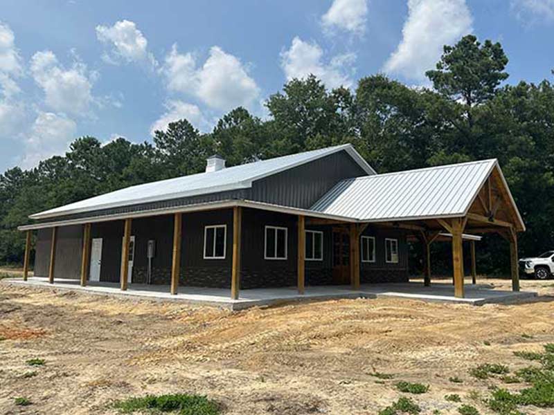 Post-frame barndominium with stone wainscot, timber porch posts and a metal roof